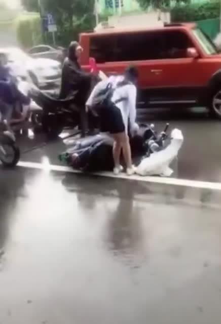 雨中女生骑车摔倒,外卖小哥帮忙把女生扶起 